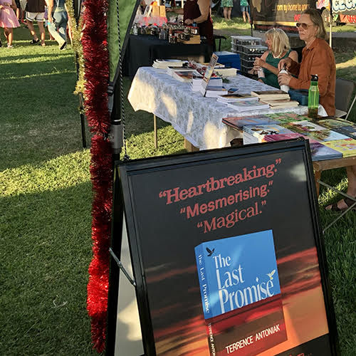 Author market stall at 2023 Bulimba Community Christmas Markets Author market stall at 2023 Bulimba Community Christmas Markets. Terrence and fellow author Tracey Dunn sitting at the table with their books. The Last Promise advertising sandwich board is in the foreground.
