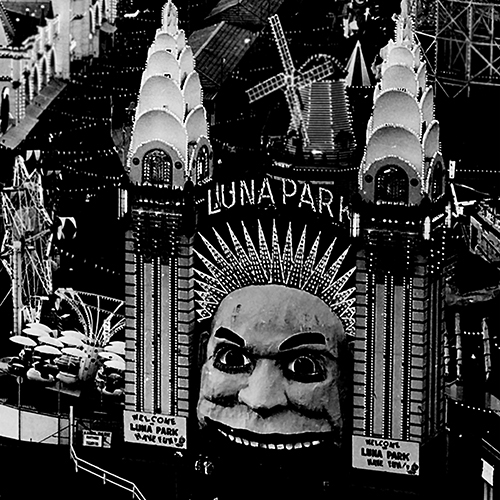 Historical photograph of the iconic entrance to Sydney Luna Park. Two Art Deco spires rise either side of the entrance, a giant garish smiling face. Glittering lights edge every contour, creating a sparkling array. Historical photograph of the iconic entrance to Sydney Luna Park. Two Art Deco spires rise either side of the entrance, a giant garish smiling face. Glittering lights edge every contour, creating a sparkling array.