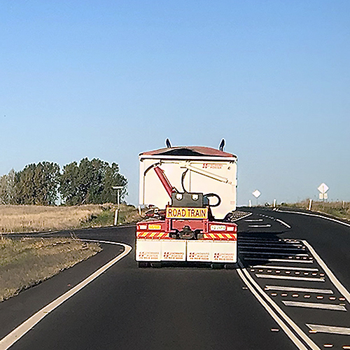 Road Train Out ahead through the windshield, the rear of a road train blocks the view of the open road as we crest a hill, making one vulnerable to the sudden surprise of who knows what